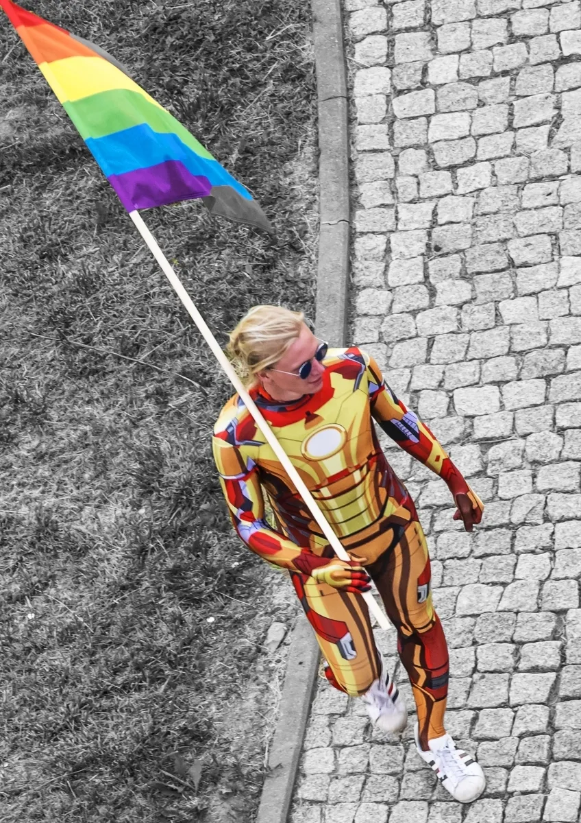Performer in a metallic rainbow costume carrying a rainbow flag